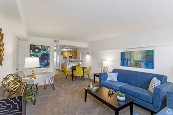 A living room with a blue couch and yellow chairs and a dining room table